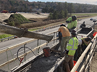 Three workers guide concrete being poured into support wall.